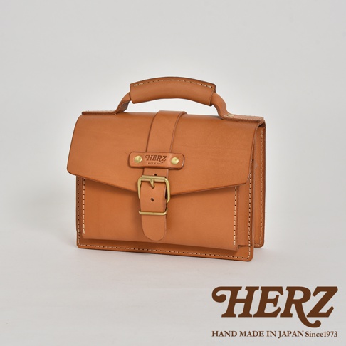 棕褐色皮革迷你單肩包，帶有提把、翻蓋、金屬釦帶及品牌標誌。