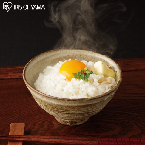 陶瓷碗中盛有熱騰騰的越光米飯，米飯上方放著一顆鮮黃的生雞蛋黃，點綴著蔥花，旁邊還有幾塊奶油。碗的材質為粗糙的陶土，顏色呈現米白色與深棕色交織。