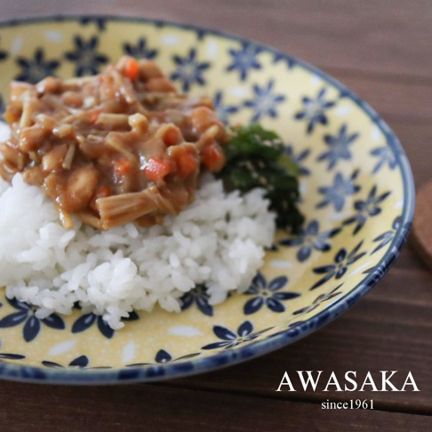 一個黃色淺湯盤，飾有藍色花卉圖案，盤中盛有白飯、淋上肉醬與蔬菜的料理，以及一小撮綠色蔬菜。