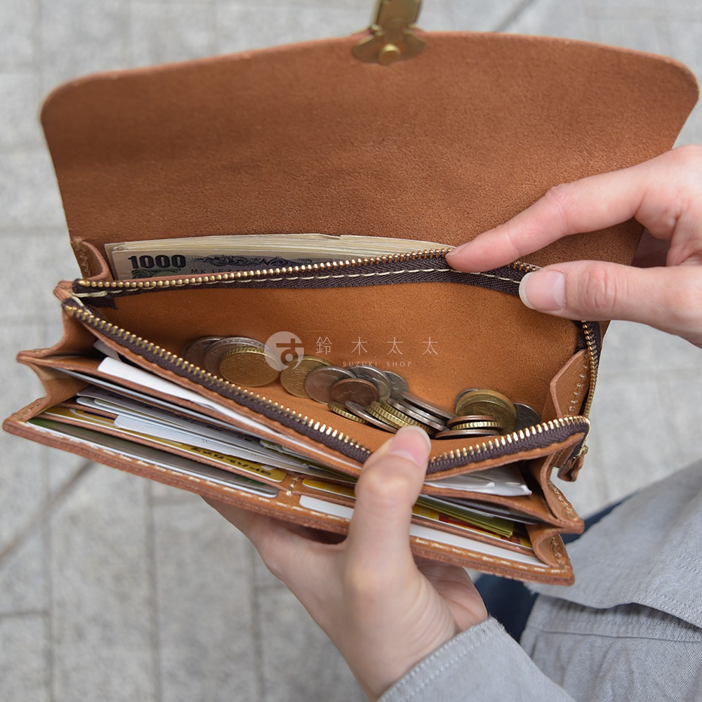 職人手作皮革長夾，手風琴式多卡層設計，展現原色皮革紋理，內有鈔票、硬幣及多張卡片，由雙手持握，展示其容量與實用性。