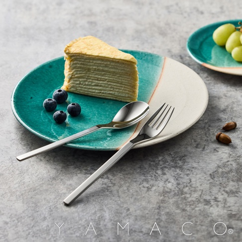 銀色不鏽鋼叉匙組，搭配藍綠色釉彩盤上的千層蛋糕與藍莓，旁為另一盤綠葡萄，整體呈現精緻的餐食擺設。