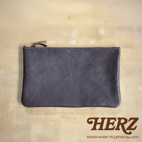 深棕色職人手作皮革拉鍊式小物收納袋，帶有金色拉鍊和皮革拉頭，表面有自然皮革紋理。