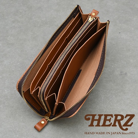 HERZ 品牌標誌，下方有 HAND MADE IN JAPAN Since1973 字樣，圖片主體為一個打開的棕色皮革長夾，內部隔層清晰可見。