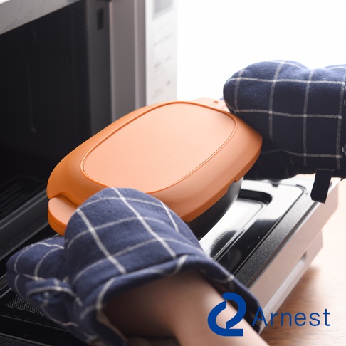 Arnest 多功能快速微波料理器，使用者戴著藍白格紋隔熱手套，從微波爐中取出一個橘色的蓋子，蓋子上有一個手柄。