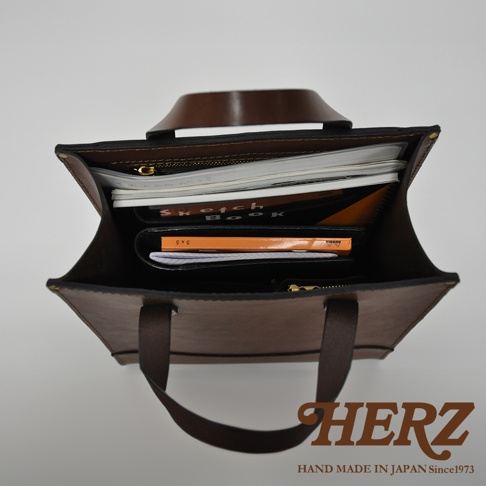 職人手作皮革直式托特包，深棕色皮革，包內裝有筆記本、文件夾等物品。