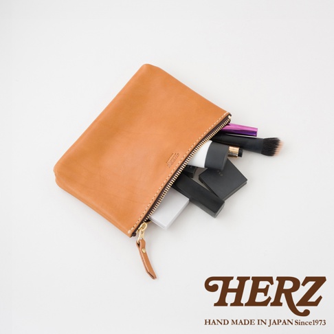 職人手作皮革長方形拉鍊收納包，淺棕色，拉鍊開口露出化妝品，包含粉餅、唇膏及化妝刷。