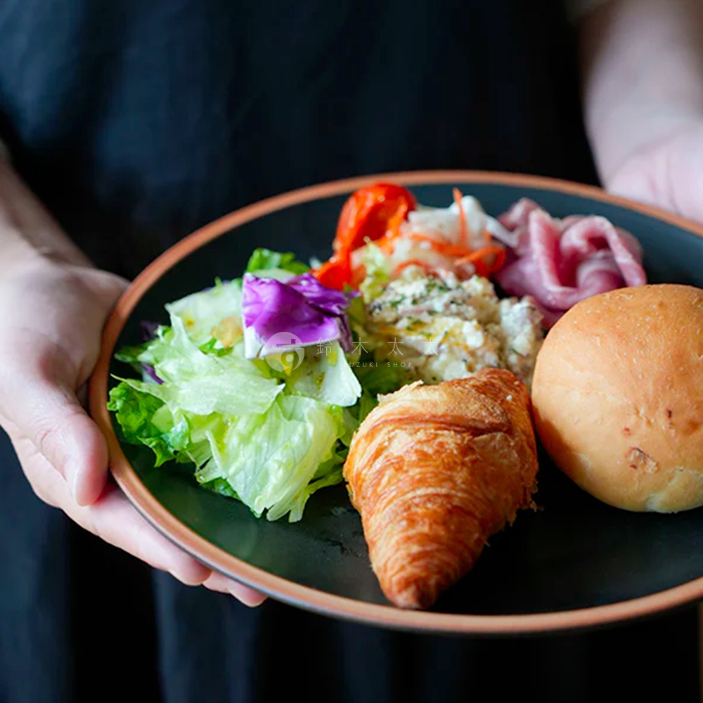 黑色陶瓷主菜盤盛有早餐，包含可頌、麵包、沙拉、火腿和馬鈴薯沙拉。