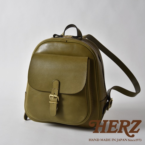一只橄欖綠色的職人手作皮革迷你後背包，具有立體口袋、金色扣環和拉鍊，以及可調節的肩帶。