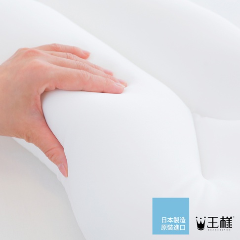 一隻手輕壓白色柔軟的雲上枕，枕頭呈現曲線設計，材質看起來蓬鬆有彈性。右下角有「日本製造 原裝進口」的藍色方塊標誌和「王樣」品牌 logo。