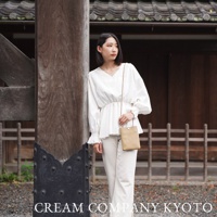 淺棕色皮革製成的簡約直立式手機包，配有細長肩帶，由一位身穿白色上衣和米色長褲的女性展示。