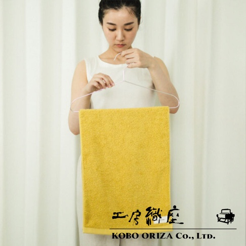 一名女子手持衣架，展示一條亮黃色的超細纖維毛巾，毛巾材質蓬鬆，具有高密度觸感。