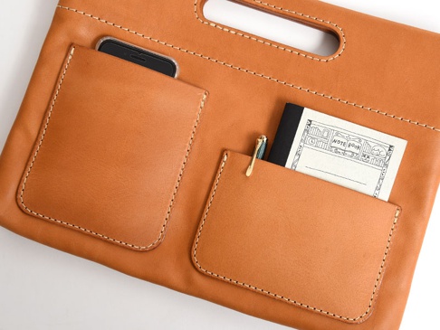 職人手作皮革橫式收納袋中袋，採用淺棕色皮革製成，配有兩層外袋，分別裝有一支手機和一本筆記本及一支筆。整體車縫線明顯。