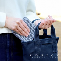 手持一塊藍白條紋、織紋明顯的方巾，正在放入一個深藍色帆布托特包。