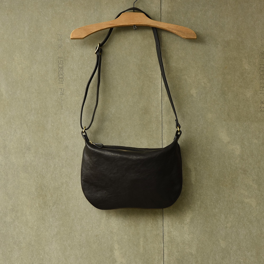 黑色皮革製成的半月形單肩包，配有可調節肩帶和金色拉鍊。