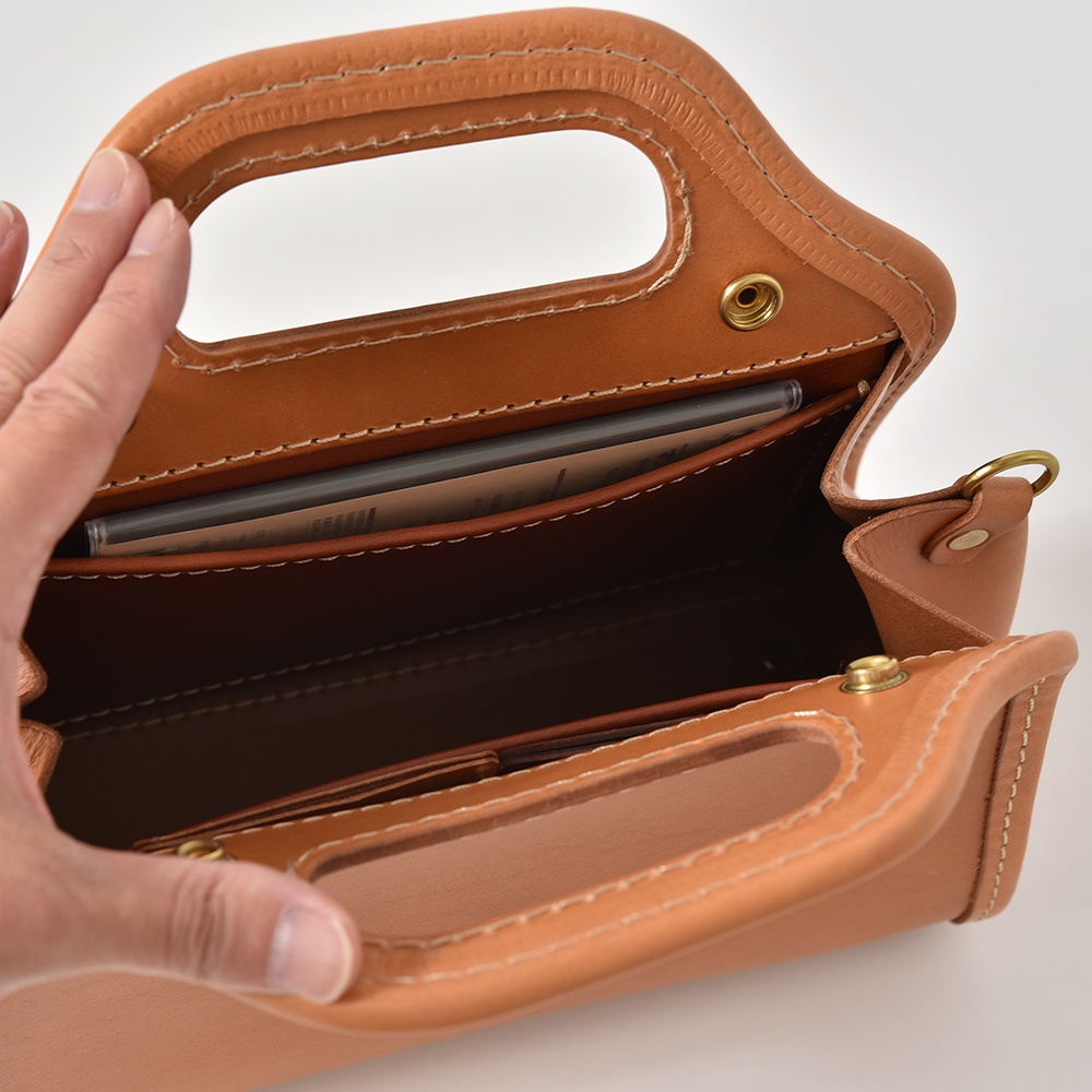 職人手作皮革單肩兩用拱型手袋，採用原色皮革製作，搭配米白色縫線。手袋內部可見手機及卡片，設有內袋及金屬釦。