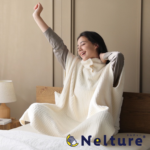 一位年輕女子穿著奶油色連帽斗篷，在床上伸懶腰。