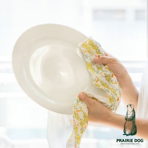 一隻手拿著白色圓盤，另一隻手用印有黃色和橙色小花的五層紗擦拭巾擦拭圓盤。
