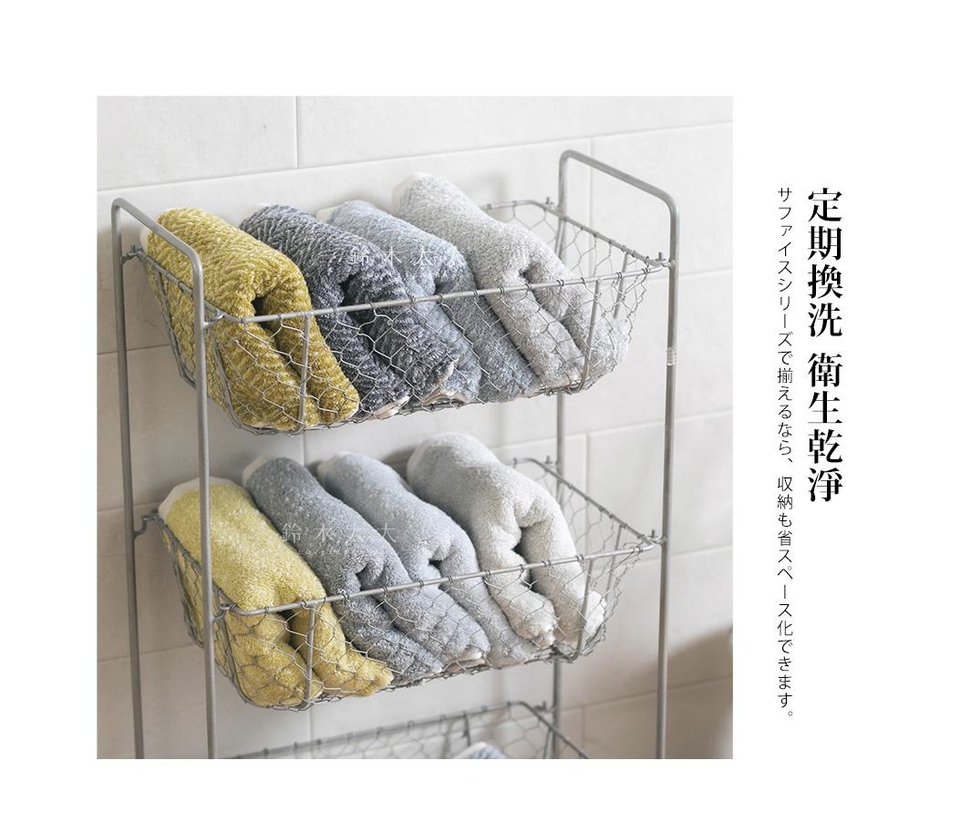 架子上擺放著兩層的 SUFFICE 棉麻混紡毛巾，包含黃色、淺灰色、深灰色和白色，質感柔軟，適合日常使用。