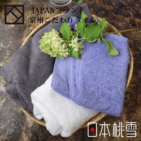 籃子裡疊放著三條加厚毛巾，分別是深灰色、淺紫色和白色。毛巾材質柔軟，表面有細緻的絨毛，並點綴著一枝淺綠色的小花束。