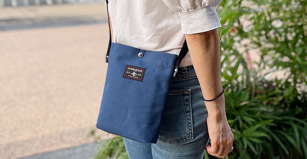 藍色帆布材質的平板收納側背包，配戴在身穿白色上衣和牛仔褲的女性身上。