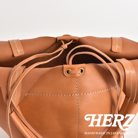 職人手作皮革球形肩掛托特包，呈現自然棕褐色，採用柔軟皮革材質，以白色縫線勾勒出包身線條，並以皮革繫帶束口，整體散發簡約質感。