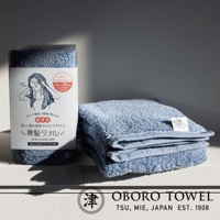 藍色五倍吸水專髮擦髮巾，材質為棉，觸感柔軟，尺寸為 33x90公分，包裝盒上有女性使用擦髮巾的插畫，旁邊疊放著兩條同款擦髮巾。