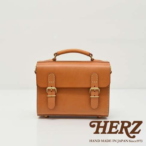 棕褐色皮革製成的迷你兩用包，帶有可調節的肩帶和頂部提把。包身正面有兩個搭扣設計，整體呈現簡約風格。