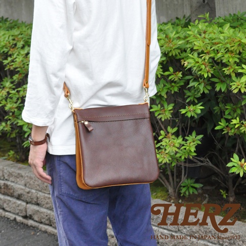 職人手作皮革翻轉雙色直式斜背包，深棕色皮革包身搭配淺棕色側邊，簡約設計，附有拉鍊小袋。