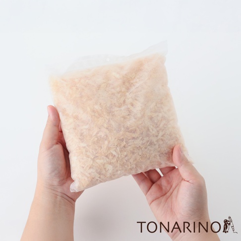 雙手捧著一個半透明的淺米色布袋，袋內裝滿了淺棕色的檜木屑。