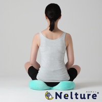 一位女性從後方視角坐著，她穿著灰色細肩帶背心和黑色短褲，坐在一個土耳其藍色的瑜珈感舒壓美姿矯正坐墊上，坐墊的下方可以看到品牌名稱 Nelture。