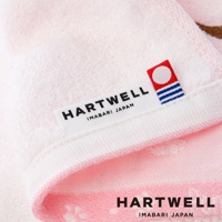 淺粉色純棉條紋紗布浴巾，邊緣有「HARTWELL IMABARI JAPAN」品牌標籤及紅藍配色小旗幟圖案。