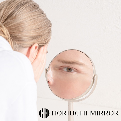 香檳金桌上型化妝圓鏡，鏡框為金屬材質，可旋轉調整角度，鏡面清晰映照出一位女性的眼部特寫。