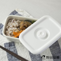 長方形白色琺瑯保存容器，內含米飯、炸物、茄子及紅蘿蔔絲，容器蓋為白色，上有圓形氣閥設計，置於藍白條紋布上，旁有木筷。