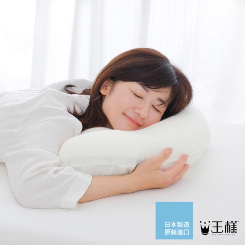 一名女子側臥，臉部朝右，閉眼微笑，頭枕在一個柔軟的白色枕頭上，枕頭呈現曲線造型，材質看起來像棉或記憶泡棉，女子穿著白色寬鬆睡衣。