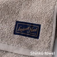 Landwell Hotel 泉州精繡長纖匹馬棉浴巾，米灰色，表面織有細緻絨圈，左側繡有Landwell Hotel品牌標誌的深藍色布標。