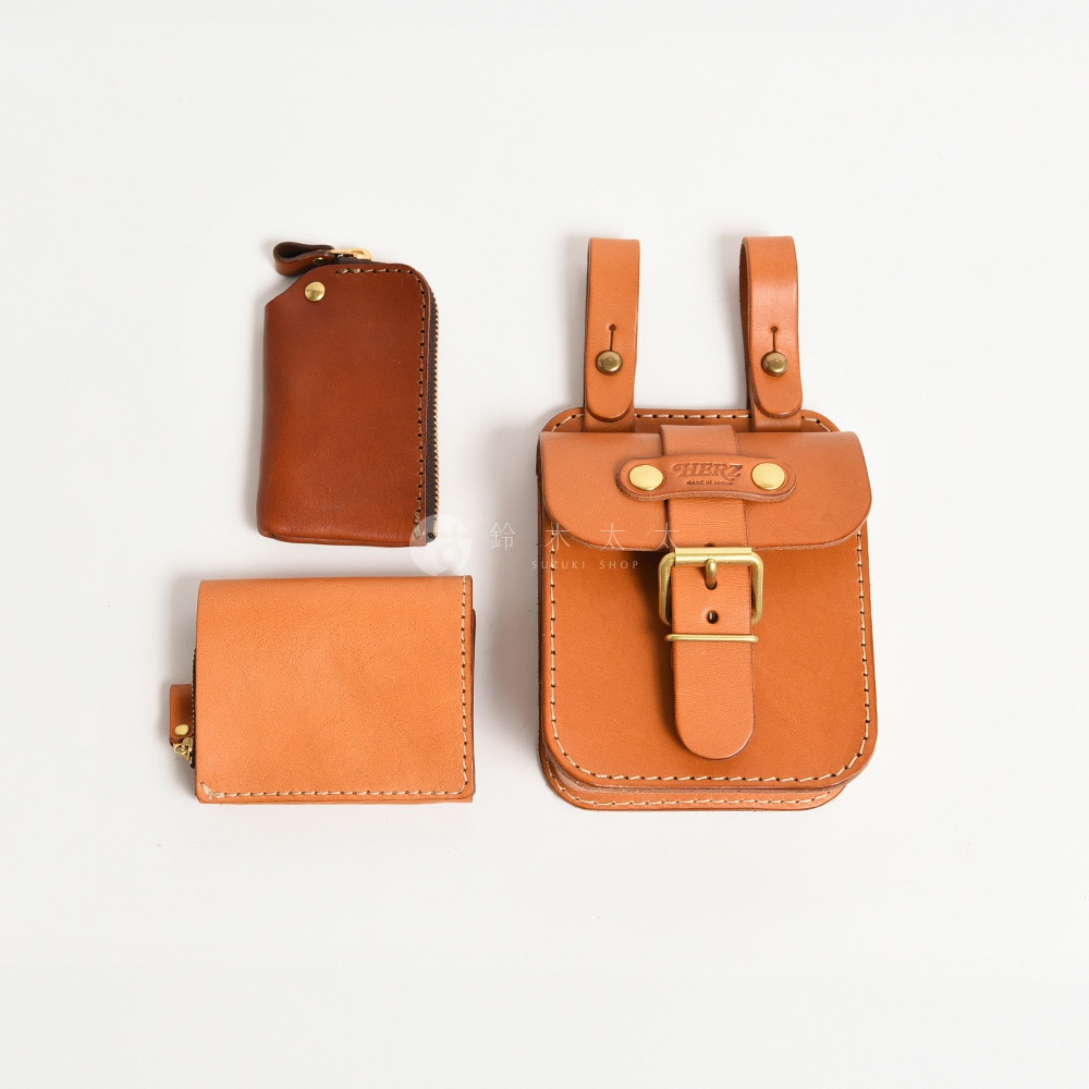 皮革製品組：一個棕褐色拉鍊零錢包、一個淺棕色摺疊式皮夾，以及一個附有皮帶扣的棕褐色腰掛包，均為手作牛皮製品。