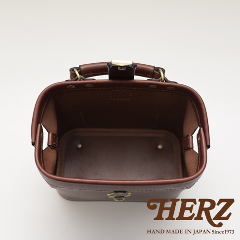 職人手作皮革方型迷你醫生包，呈現深棕色調，包身結構方正，配有金屬旋鎖和手提把，內部空間寬敞，展現皮革的自然紋理和精緻車縫工藝。