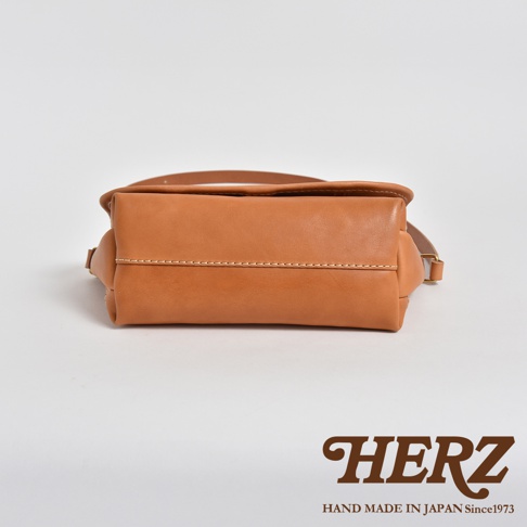 職人手作皮革復古郵差包，採用淺棕色皮革製作，包身線條簡潔，縫線明顯，展現細緻工藝。