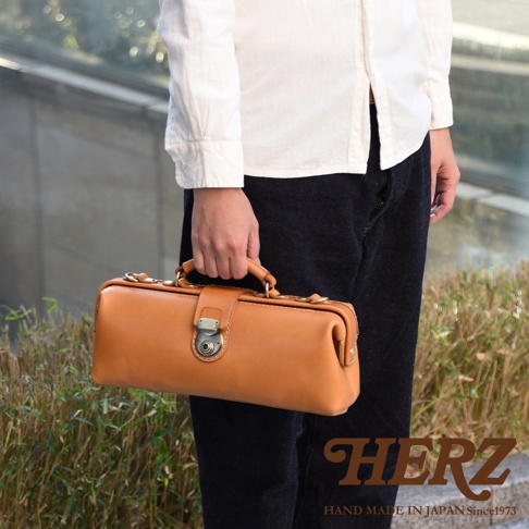 日本HERZ品牌手工製作的淺棕色皮革長形手提包，由一人手持。