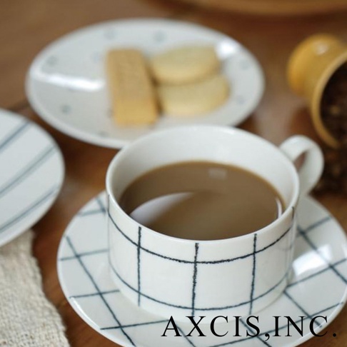 一只裝有咖啡的白色陶瓷馬克杯，杯身與杯碟均印有黑色手繪格紋。背景有餅乾和咖啡豆。