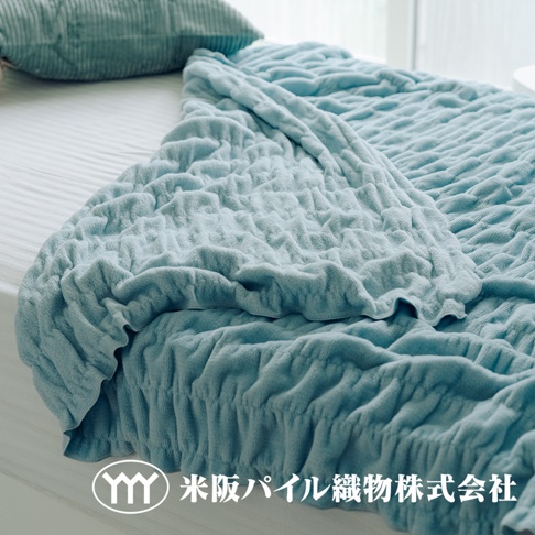 淺藍色輕暖柔蓬抗摩四季毯，細緻的立體紋理，柔軟的材質，搭配同色系燈芯絨抱枕，置於白色床鋪上。