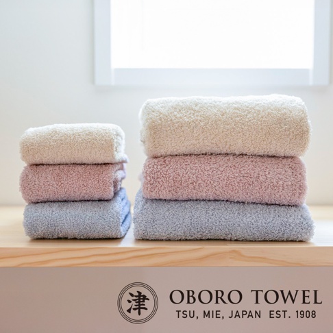 堆疊的有機棉毛巾，呈現米白色、粉紅色和淺藍色，質地柔軟蓬鬆，展示於木質檯面上。