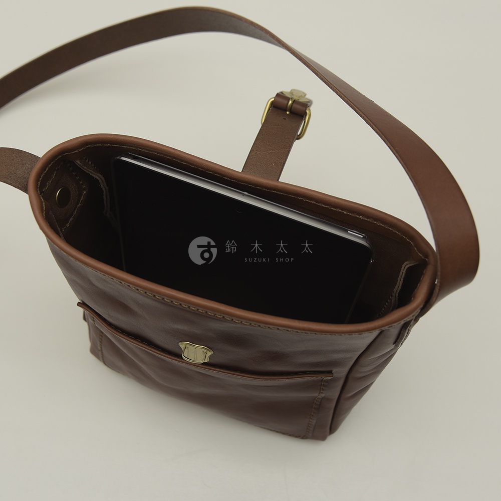 棕色皮革手作單肩側背包，包內可見一台黑色平板電腦，包身有翻蓋前袋，配有金屬釦，可調節的皮革肩帶。