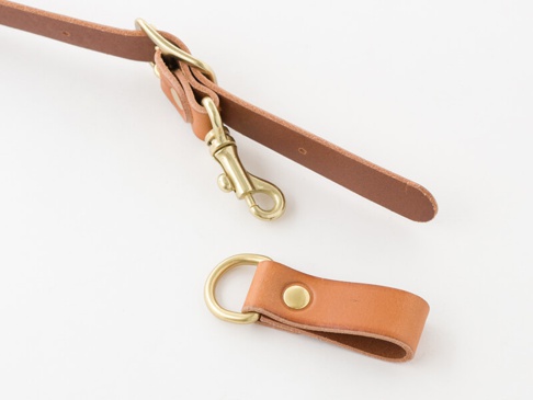 職人手作皮革背包用胸前扣帶，由淺棕色皮革製成，寬2.4公分。扣帶末端有一個黃銅色鉤扣，另一端有一個附有黃銅色D型環的皮革環。
