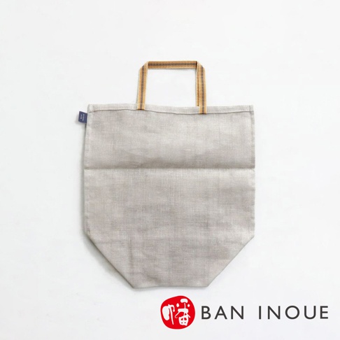 淺灰色棉麻材質提把收納袋，有兩條木質紋理提把，袋身下方有菱形縫線設計，左側有藍色小標籤。