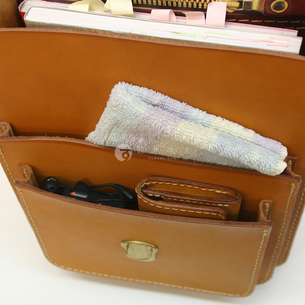 職人手作皮革單肩兩用小方包 A-10，以淺棕色皮革製成，包內有文件、毛巾、耳機及皮夾。