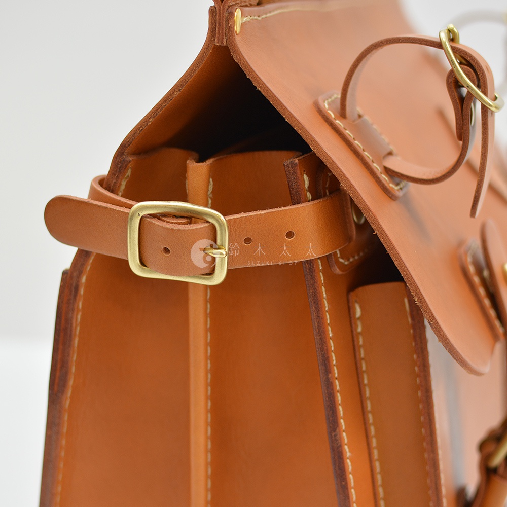 職人手作皮革旅行包，側邊特寫，展示棕色皮革材質、黃銅釦環及車縫線細節。