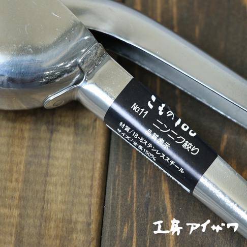 銀色不鏽鋼壓蒜器，帶有黑色標籤，標示「No.11 壓蒜器」、「材質/18-8不鏽鋼」、「尺寸/全長150mm」。