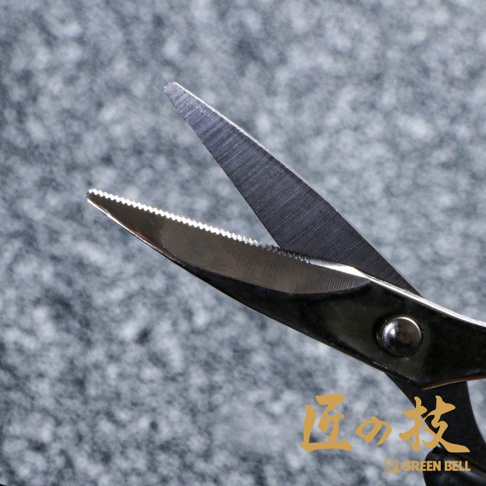 特寫不鏽鋼指甲剪，剪刀刃部有細緻的鋸齒紋路，剪刀柄為銀色金屬材質，背景為灰色紋理。