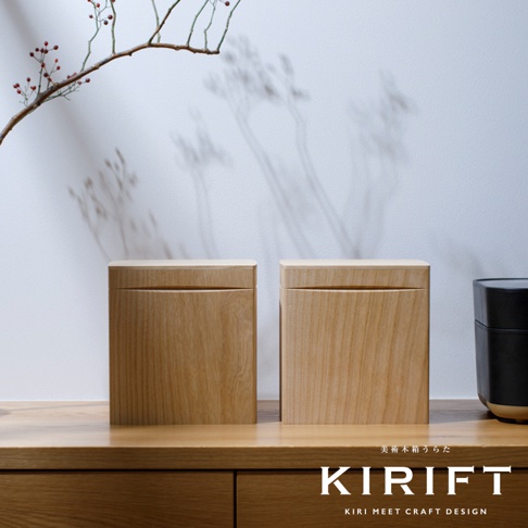 兩個淺木色桐木調濕儲米箱，方形設計，表面有自然木紋。箱蓋與箱體緊密結合，風格簡約。背景為白色牆面，左側有帶紅色漿果的枯枝。